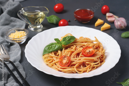 Spaghetti with tomato sauce and cherry tomatoes with basil on white plate on dark background. Closeup