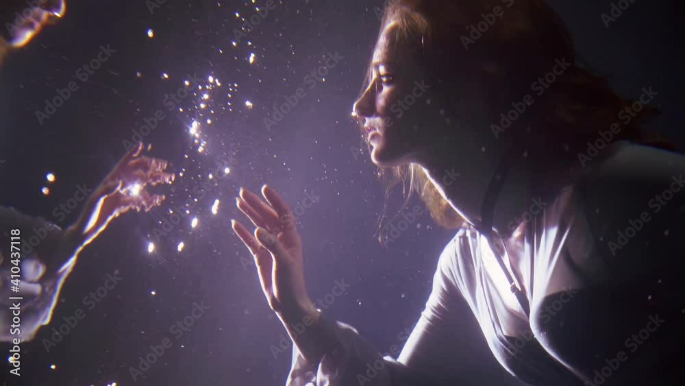 magic underwater shot of young woman floating in depth and looking on her reflection in water mirror