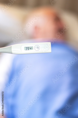 Persona de tercera edad al fondo y en primer plano un termómetro indicando alta temperatura