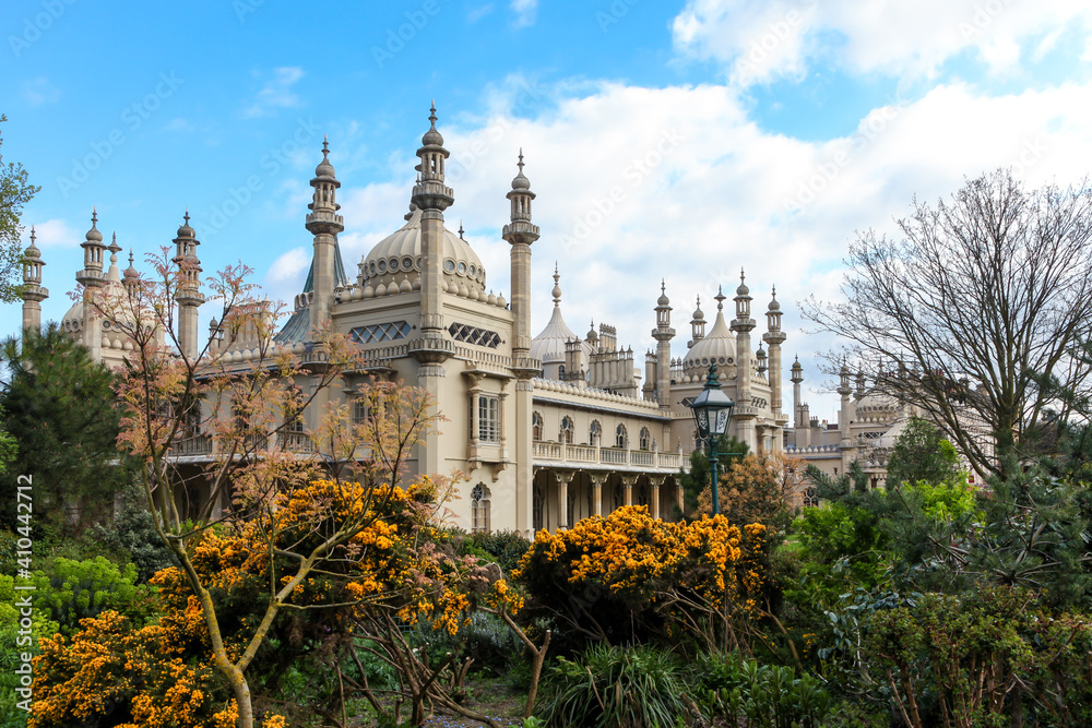 Beautiful view of the majestic Brighton Royal Pavilion from the English style garden full of plants and flowers on sunny summer day with blue sky. Concept of architecture, culture, art, gardening.