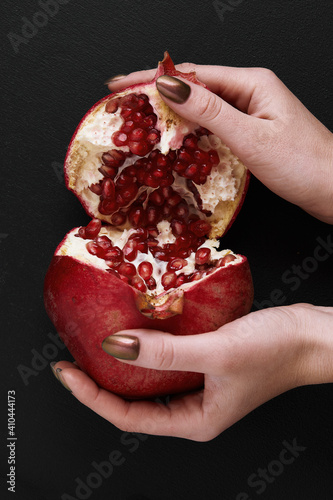 female hands breaking pomegranate in half on black background
