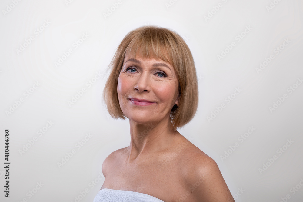 Aging gracefully. Beauty portrait of senior lady wearing towel, having silky skin, looking at camera on light background