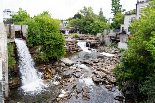 Almonte Falls, Ontario, Canada, a tiered and multiple segmented waterfall, surrounding small trees and grasses on bedrock during summer.