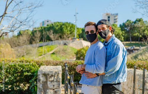 Gay Couple Wearing Protective Face Mask Looking at Camera Hugging at Padlock Bridge