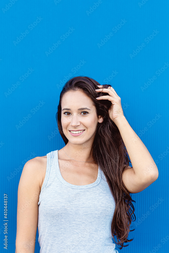 Portrait of a beautiful young woman smiling and playing with her hair with a blue background
