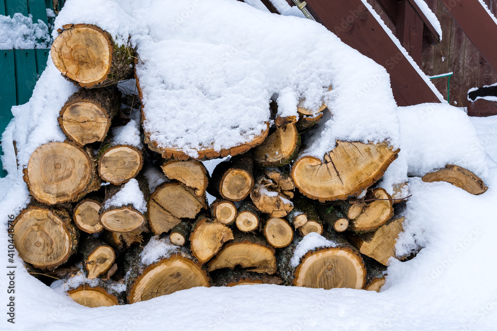 Oak logs stacked in a woodpile near the house as firewood for heating Oak logs stacked in a woodpile near the house as firewood for heating