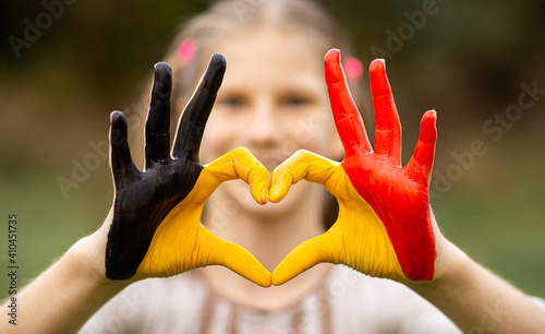 Kid hands painted in Belgium flag color show symbol of heart and love gesture on nature background. Focus on hands photo