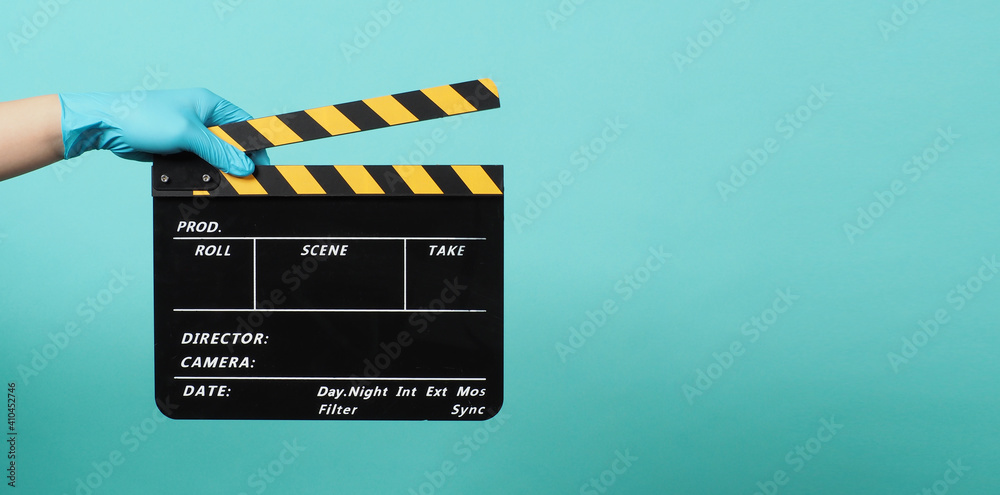 Hand is wear glove and hold Yellow Clapperboard or movie Clapper board for videography. it use in video production ,movies and cinema industry on green Tiffany Blue background.director film slate