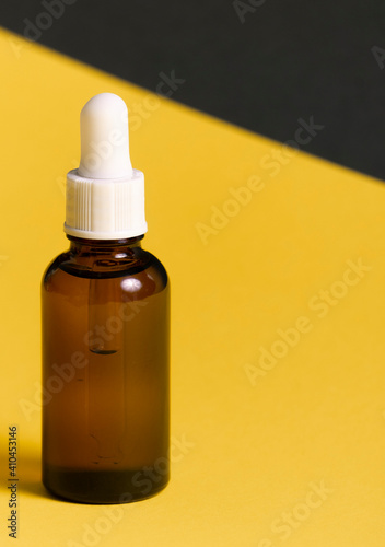 selective focus. a glass jar with a pipette. inside is a cosmetic organic oil for the skin of the face and body. on a yellow-gray paper background. copyspace