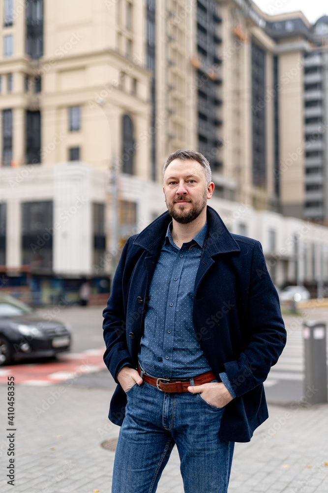 Fototapeta premium Trendy handsome man in gray coat and dark suit. Autumn city blurred background.