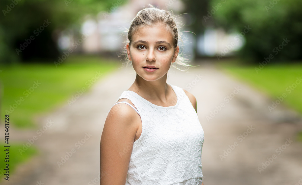 Beautiful portrait of a blond girl looking at the camera. She is wearing a white dress, has her hair attached and is smiling. Outdoor professional model photography. Shallow depth of field. Beautiful portrait of a blond girl looking at the camera. She is wearing a white dress, has her hair attached and is smiling. Outdoor professional model photography. Shallow depth of field.
