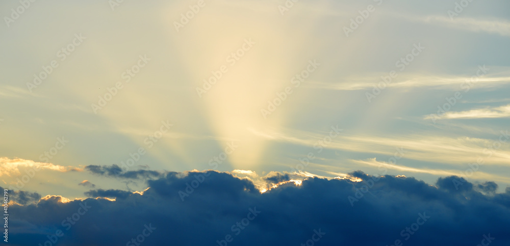 Yellow sunrays shining over clouds with blue sky