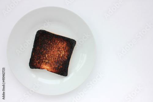 Piece of burnt toast bread on a plate on a white background. Top view, copy space