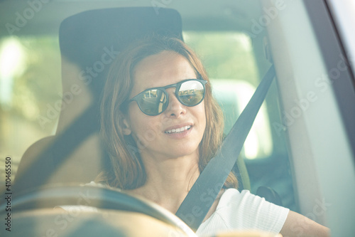 Donna chiara con  occhiali da sole guida un veicolo seduta con la cintura allacciata e con espressione rilassata photo
