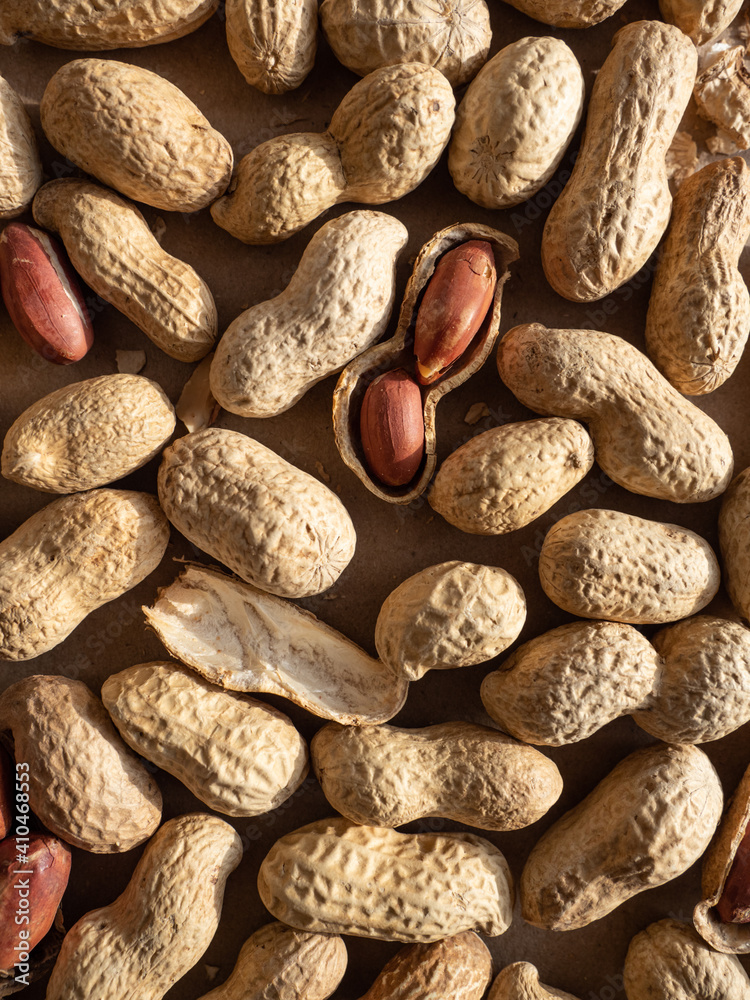 Peanuts in shells and peeled scattered on brown craft paper in the morning light Peanuts in shells and peeled scattered on brown craft paper in the morning light