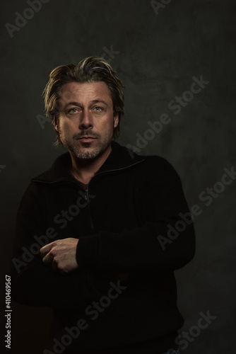 Blonde man in black woolen sweater in front of dark grey wall. © ysbrandcosijn