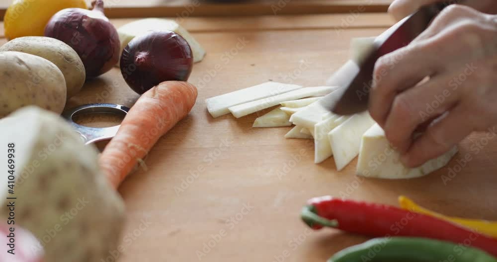 Vegetable soup preparing, chopping celery root at cutting board using sharp knife, close up