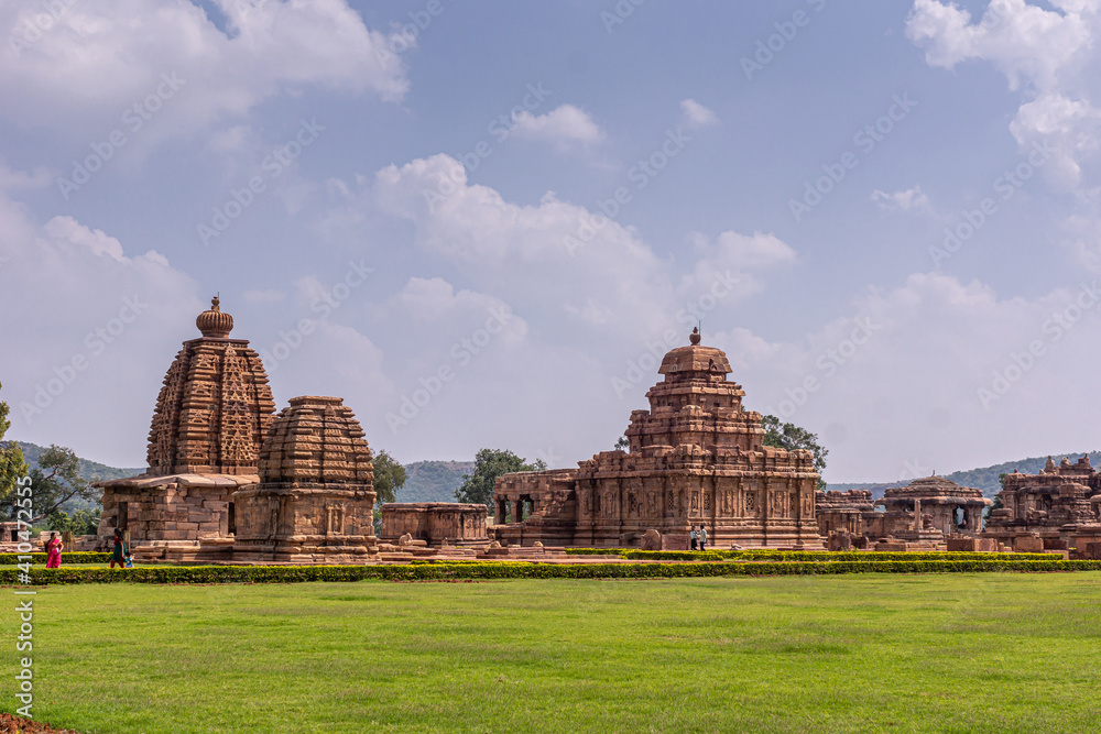 Bagalakote, Karnataka, India - November 7, 2013: Pattadakal temple complex. Green park landscape with complex of brown stone buildings set together under blue cloudscape.