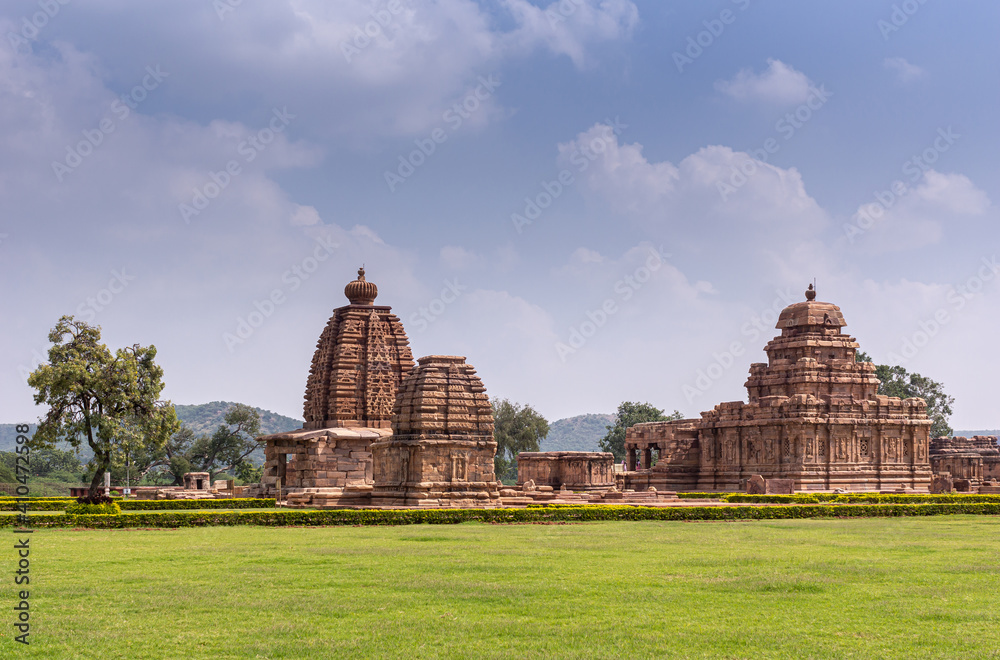 Bagalakote, Karnataka, India - November 7, 2013: Pattadakal temple complex. Wide Green park landscape with complex of brown stone buildings set together under blue cloudscape.
