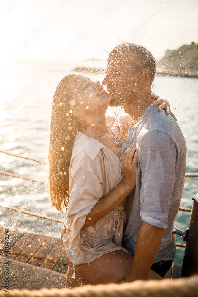 Fototapeta premium Beautiful couple in love hugs and kisses under the streams of water in a luxury spa hotel on their honeymoon, vacation in the tropics. Selective focus