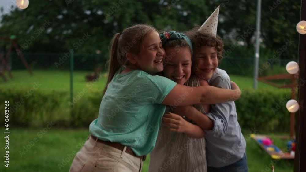 Happy teenage friends dancing and hugging at a birthday party. The birthday boy and two girls. Smartly dressed children at the birthday table outside, catering concept Happy teenage friends dancing and hugging at a birthday party. The birthday boy and two girls. Smartly dressed children at the birthday table outside, catering concept