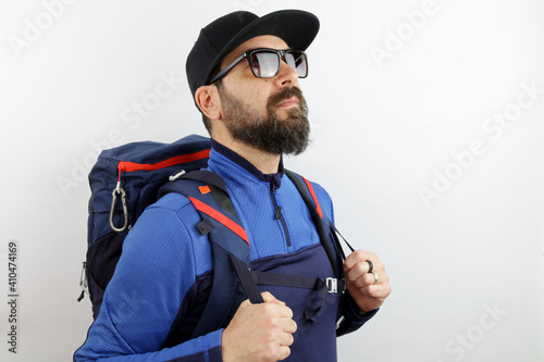 Bearded hiker with sunglasses, backpack and hat standing looking up.