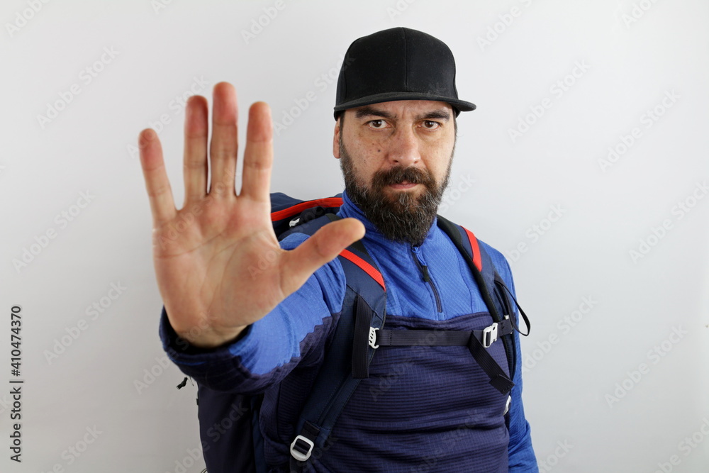 Bearded hiker with backpack and hat, doing stop sign with palm of the hand. Warning expression with negative gesture Bearded hiker with backpack and hat, doing stop sign with palm of the hand. Warning expression with negative gesture
