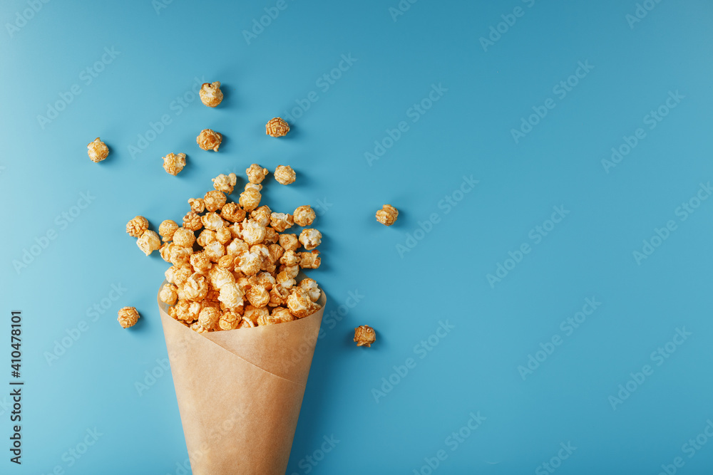 Popcorn in caramel glaze in a paper envelope on a blue background.