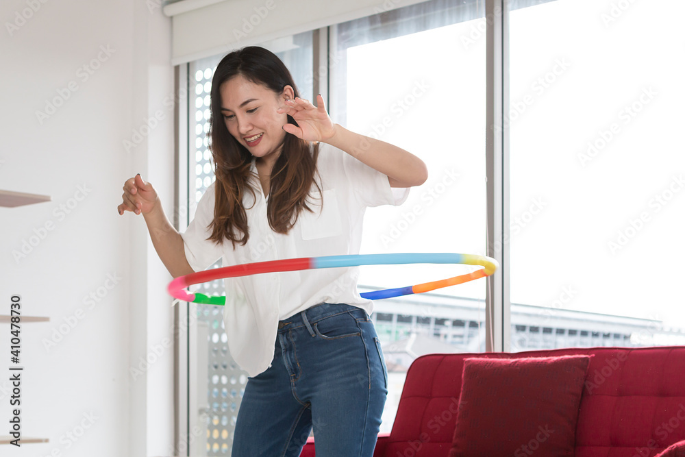Happy Asian women playing Hula Hoop in the living room at home. Young adult woman learning to play with a hula-hoop in a living room.