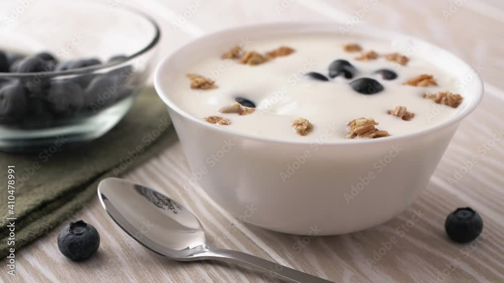 Yogurt with granola and blueberries. Adding granola and fresh blueberries into greek yogurt. Healthy breakfast or snack meal Yogurt with granola and blueberries. Adding granola and fresh blueberries into greek yogurt. Healthy breakfast or snack meal