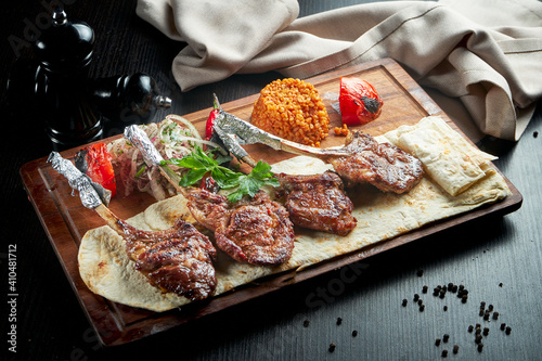 Lamb rack cooked on the grill with pita bread, bulgur and grilled vegetables on a wooden board. Turkish shashlik. Close up, selective focus