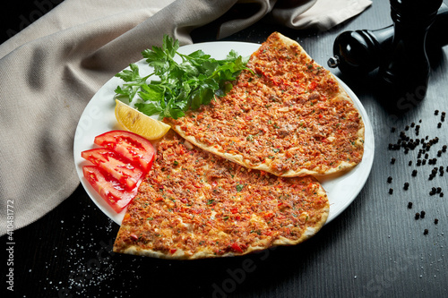 Lahmacun is a popular Turkish dish. Thin crispy tortilla with minced lamb, tomatoes and bell pepper on black background photo