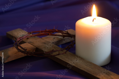 Fotografija Candle and wooden cross with thorns on violet fabric background, concept
