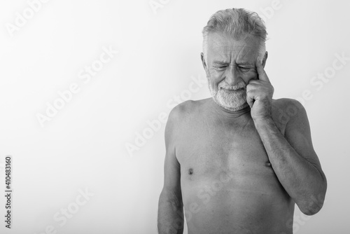Studio shot of handsome senior bearded man thinking while looking stressed shirtless against white background