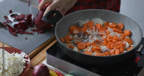 Vegetable soup preparing, peeling off  beet root while onions and carrot cooking in hot pan photo