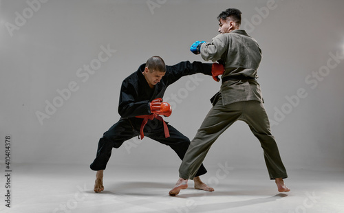 Fototapeta Naklejka Na Ścianę i Meble -  Fighting guys during mixed fight workout. Athletic males in kimono and boxing gloves training martial arts technique 