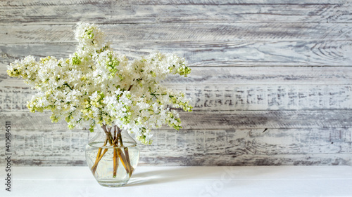 White lilac bouquet in glass vase on wooden table. Spring branches of blooming lilac festive bouquet of flowers. Long web banner with copy space.