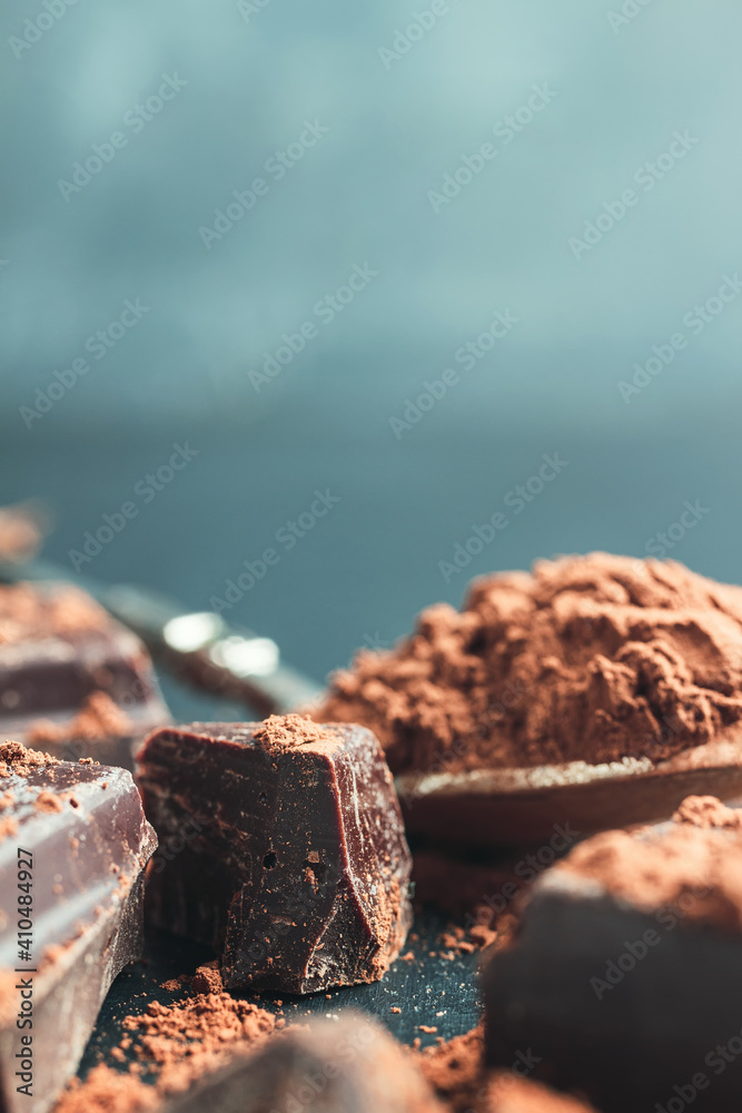 Chocolate chunk, chopped chocolate cubes with cocoa powder on dark background with copy space, close-up view Chocolate chunk, chopped chocolate cubes with cocoa powder on dark background with copy space, close-up view