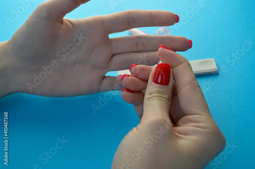 finger puncture to diagnose coronavirus. girl with red manicure makes herself an analysis on her own. finger puncture for blood sampling. girl holding a lancet and pricks her finger