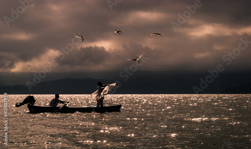Fisherman casting a net at sunset on Lake Catemaco in the Mexican state of Veracruz, with egrets circling above, hoping to catch some spoils. photo