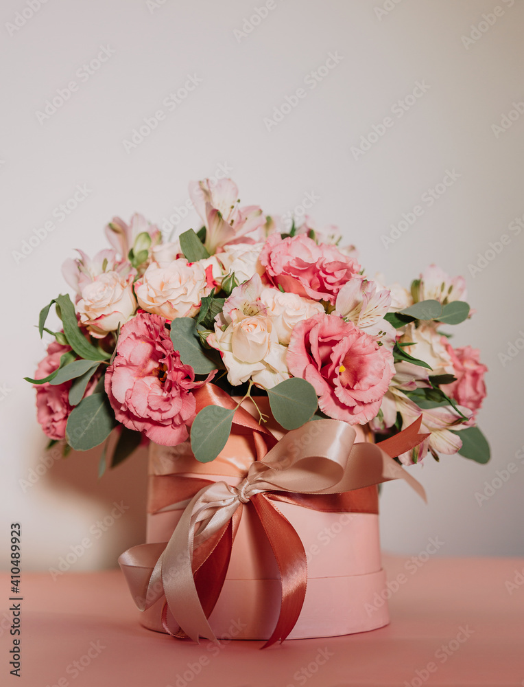 Bouquet with pink anemones and roses and eucalyptus branches in round pink box. Satin ribbon on the box. Present, spring time, happy women's day. On white background.