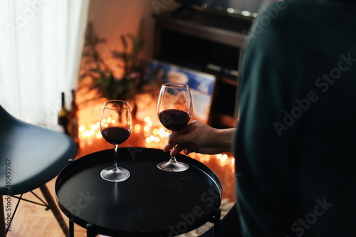 Man is holding a glass of wine. A glass of red wine is on a black table. Cosy romantic evening at home photo