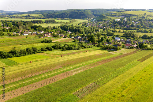 Aerial view of a small village win many houses and green agricultural fields in spring with fresh vegetation after seeding season on a warm sunny day. © bilanol