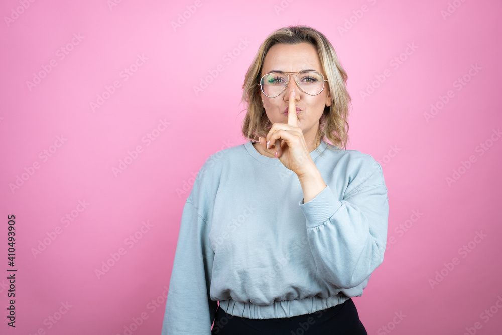 Young caucasian woman wearing sweatshirt over pink background asking to be quiet with finger on lips. Silence and secret concept. Young caucasian woman wearing sweatshirt over pink background asking to be quiet with finger on lips. Silence and secret concept.