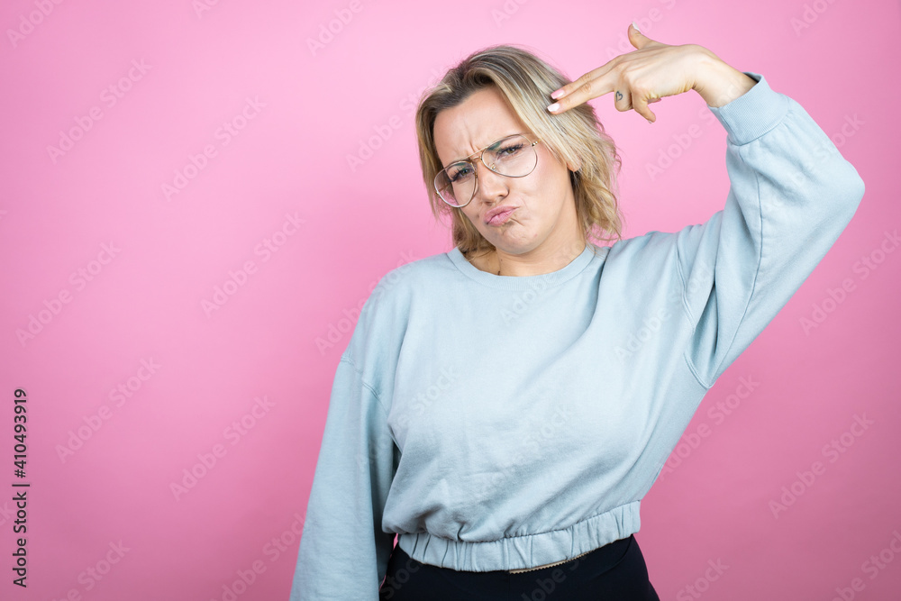 Young caucasian woman wearing sweatshirt over pink background Shooting and killing oneself pointing hand and fingers to head like gun, suicide gesture. Young caucasian woman wearing sweatshirt over pink background Shooting and killing oneself pointing hand and fingers to head like gun, suicide gesture.