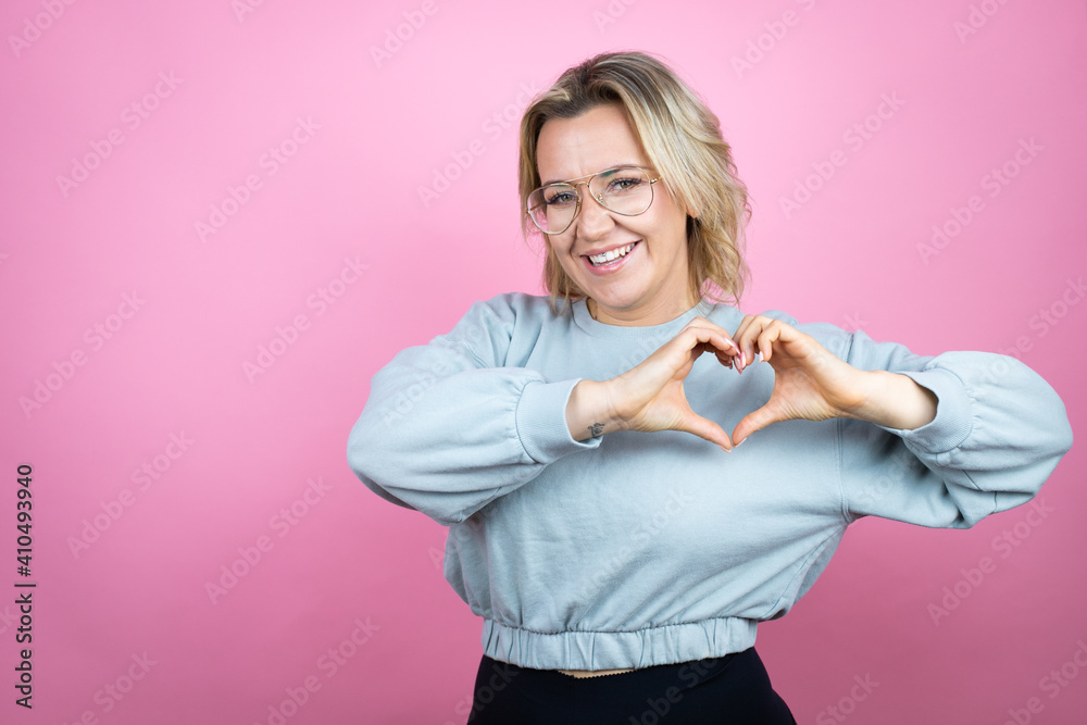 Young caucasian woman wearing sweatshirt over pink background smiling in love showing heart symbol and shape with hands Young caucasian woman wearing sweatshirt over pink background smiling in love showing heart symbol and shape with hands