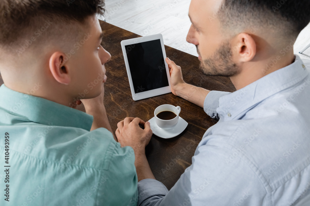 high angle view of homosexual man holding digital tablet with blank screen near husband