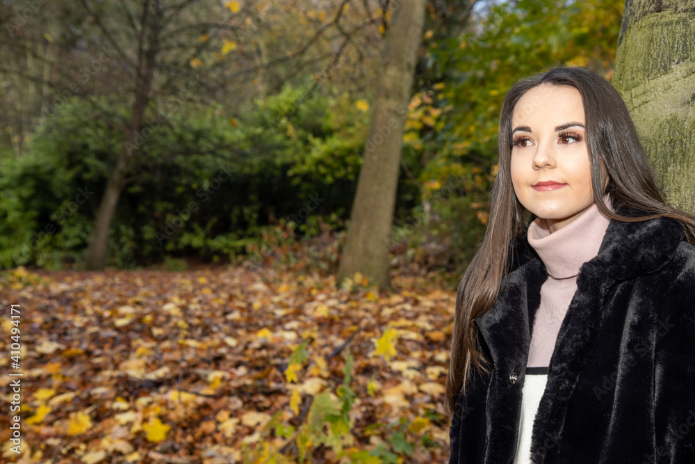 A young attractive woman with long brown hair in the winter time in a woodland park wearing a black coat A young attractive woman with long brown hair in the winter time in a woodland park wearing a black coat