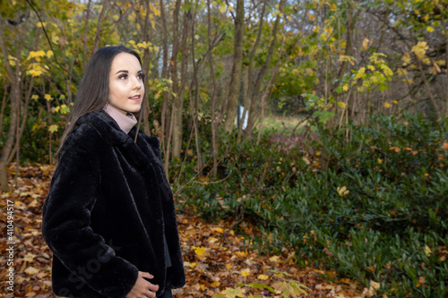 A young attractive woman with long brown hair in the winter time in a woodland park wearing a black coat