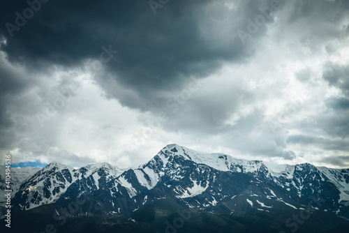 Dramatic mountains landscape with big snowy mountain ridge under cloudy sky. Dark atmospheric highland scenery with high mountain range in overcast weather. Awesome big mountains under gray clouds.